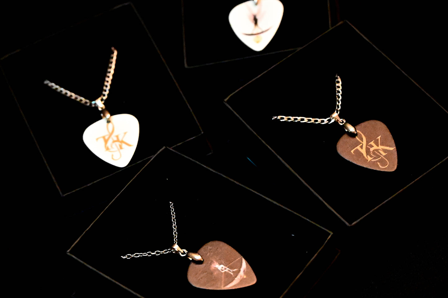 Heart-shaped plectrum necklaces with engraved designs on a black background