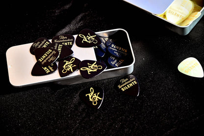Guitar picks with gold text in a white case on a dark surface
