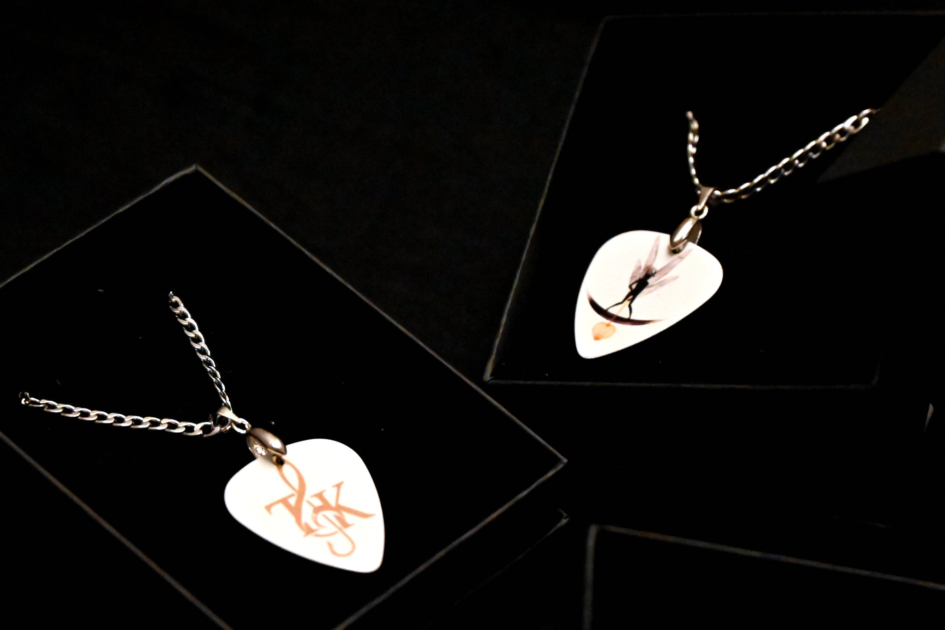 Two necklaces with guitar pick pendants on a black background