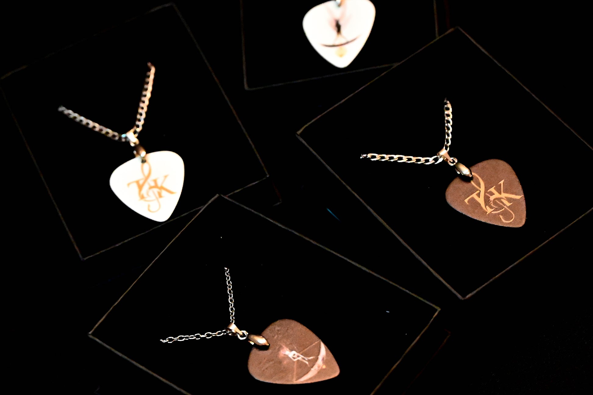 Heart-shaped plectrum necklaces with engraved designs on a black background